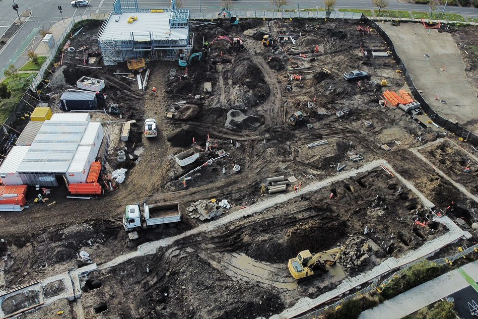 Aerial view of a large construction site with excavation work, heavy machinery, and partially built structures.